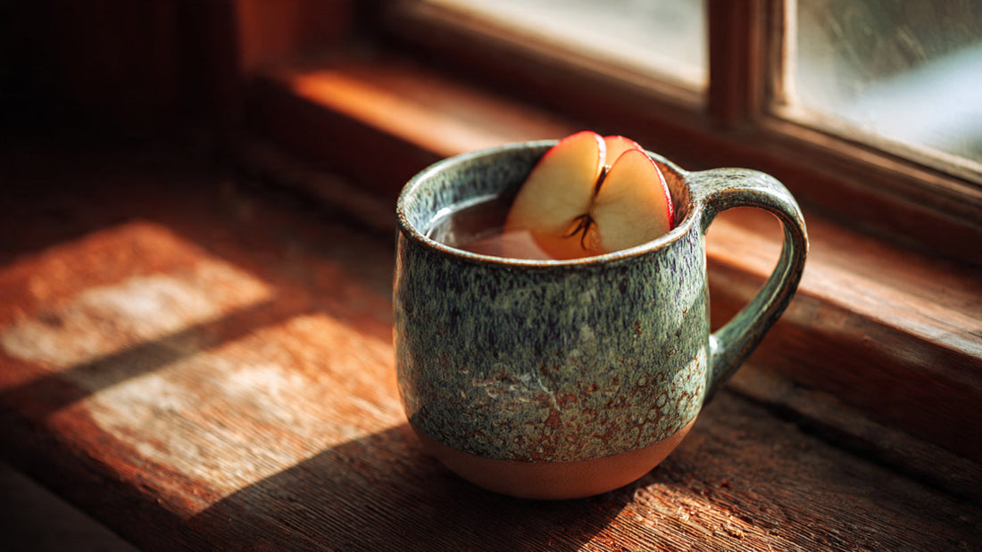 Apple rooibos tea in ceramic mug with apple slice on rustic wooden table in warm natural light
