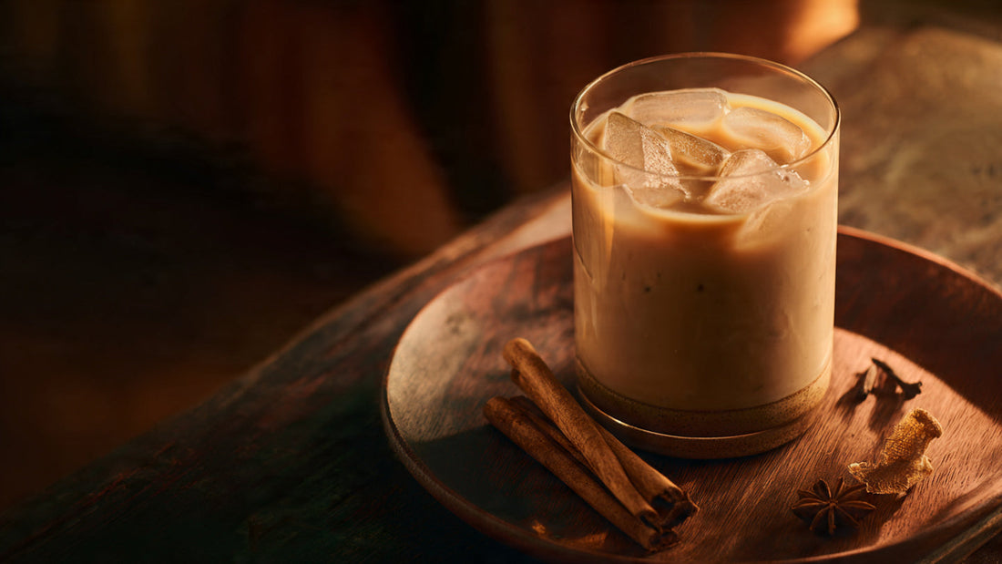 Iced masala chai latte in tall glass with cinnamon stick garnish on rustic wood table in warm natural light