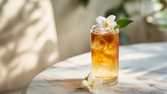 Iced jasmine tea in elegant glass with floral garnish on pale marble table in soft natural morning light