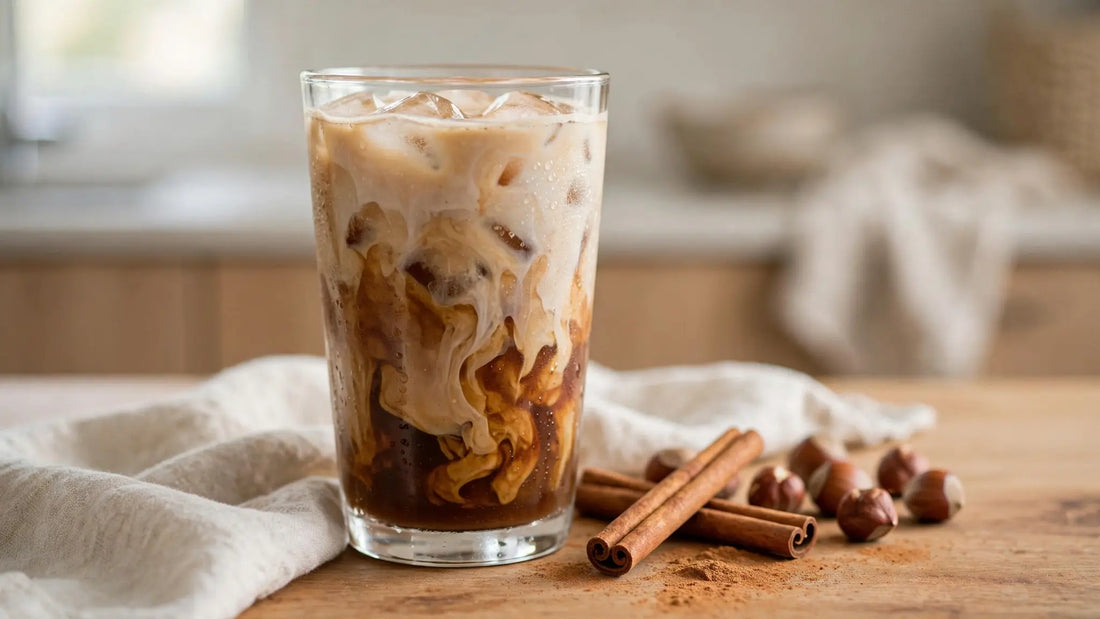 Homemade iced cinnamon hazelnut coffee in a clear glass with ice, cream layers, hazelnuts, cinnamon sticks, and a dusting of cinnamon.