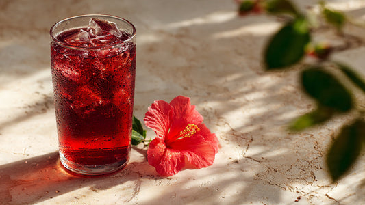 Iced hibiscus berry tea in clear glass with fresh berries on light stone table in bright natural sunlight