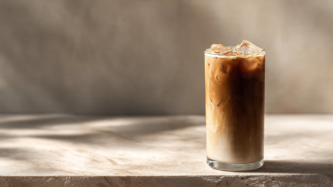 Iced hojicha latte in tall glass with warm roasted tones on neutral stone surface in soft diffused light