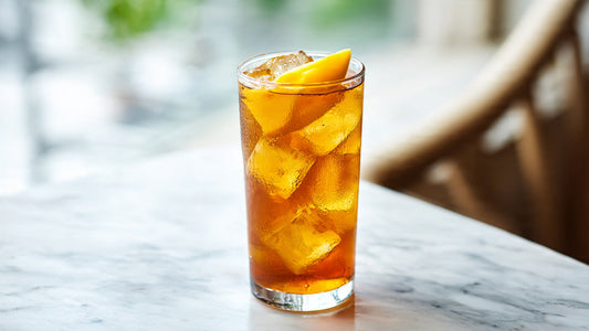 Iced mango tea in tall glass with fresh mango slice on white stone table in bright tropical sunlight