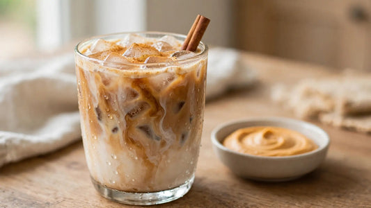 Homemade iced pumpkin spice latte in a clear glass with ice, creamy coffee layers, cinnamon sticks, and pumpkin spice on a warm kitchen counter.