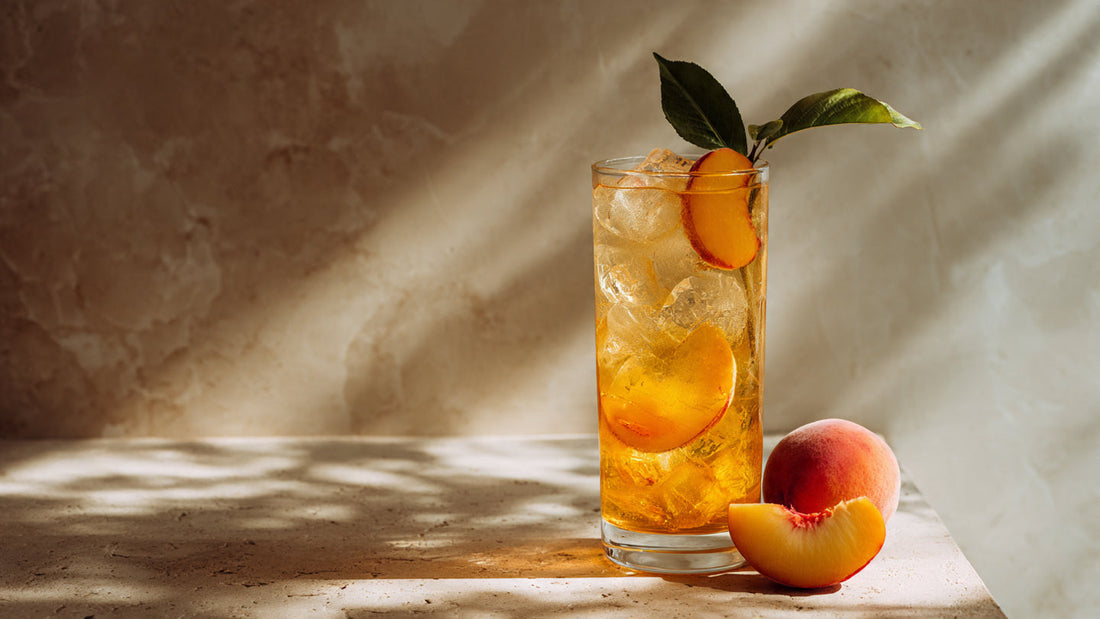 Iced peach tea in tall glass with fresh peach slice on linen table in soft summer morning light