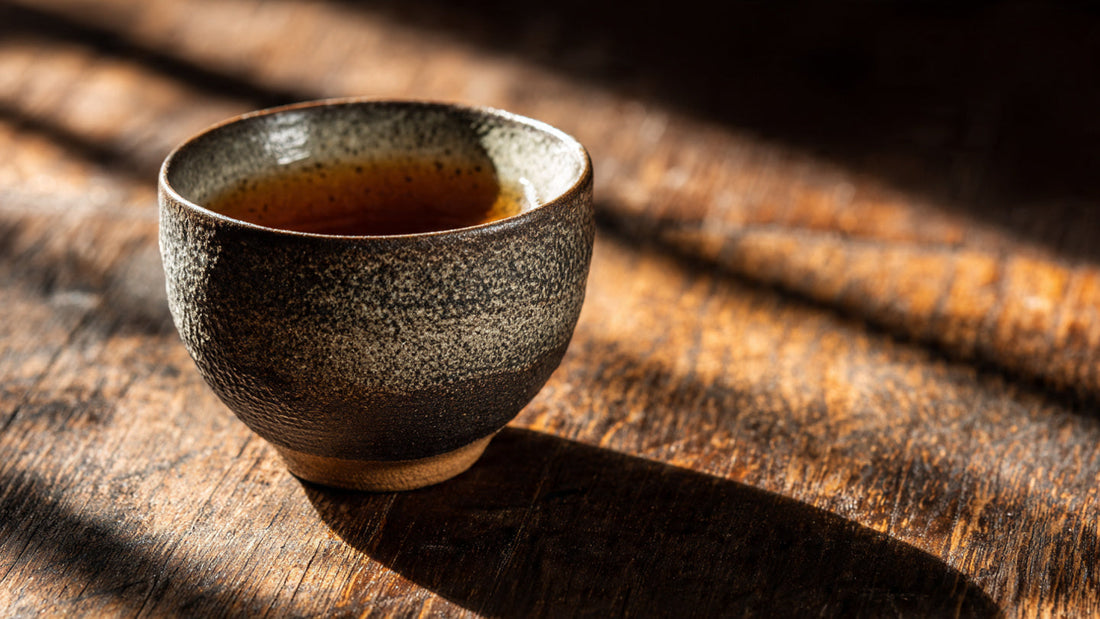 Hojicha tea in ceramic cup on dark wooden table in warm natural light