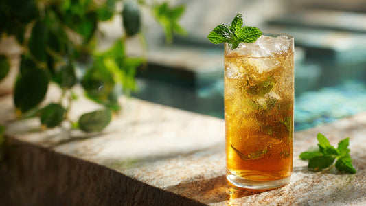 Iced Moroccan mint tea in clear glass with fresh mint sprig on light textured table in bright airy sunlight