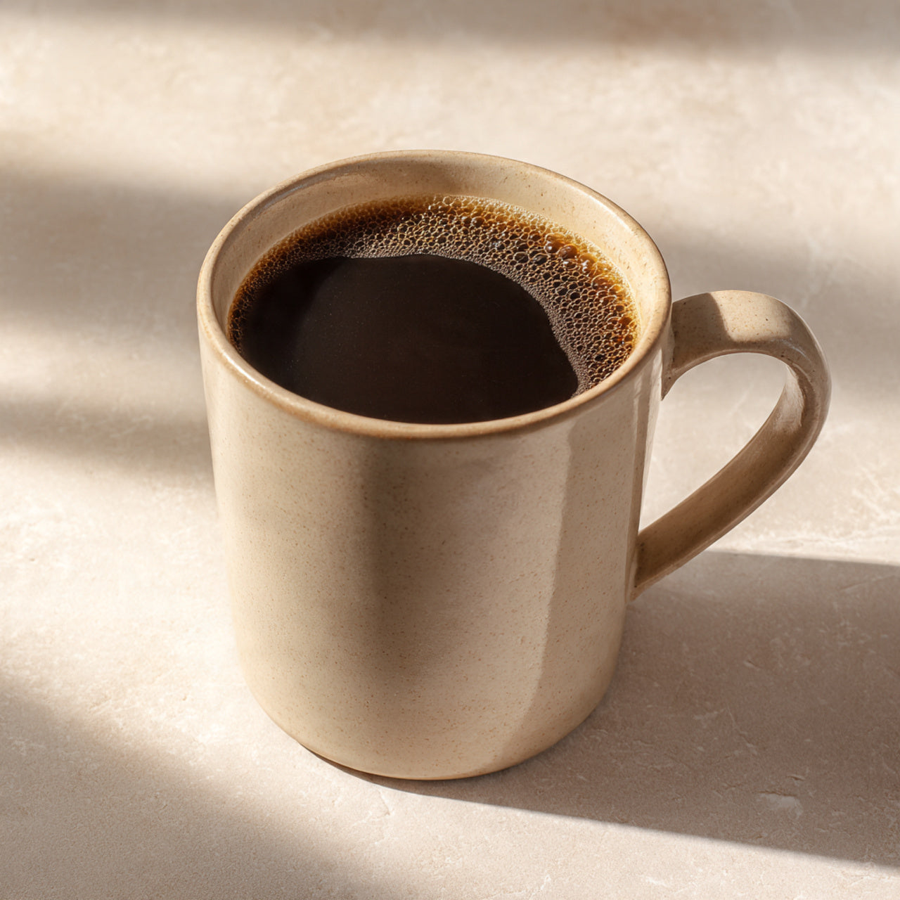 Beige ceramic mug filled with dark coffee on a light beige surface