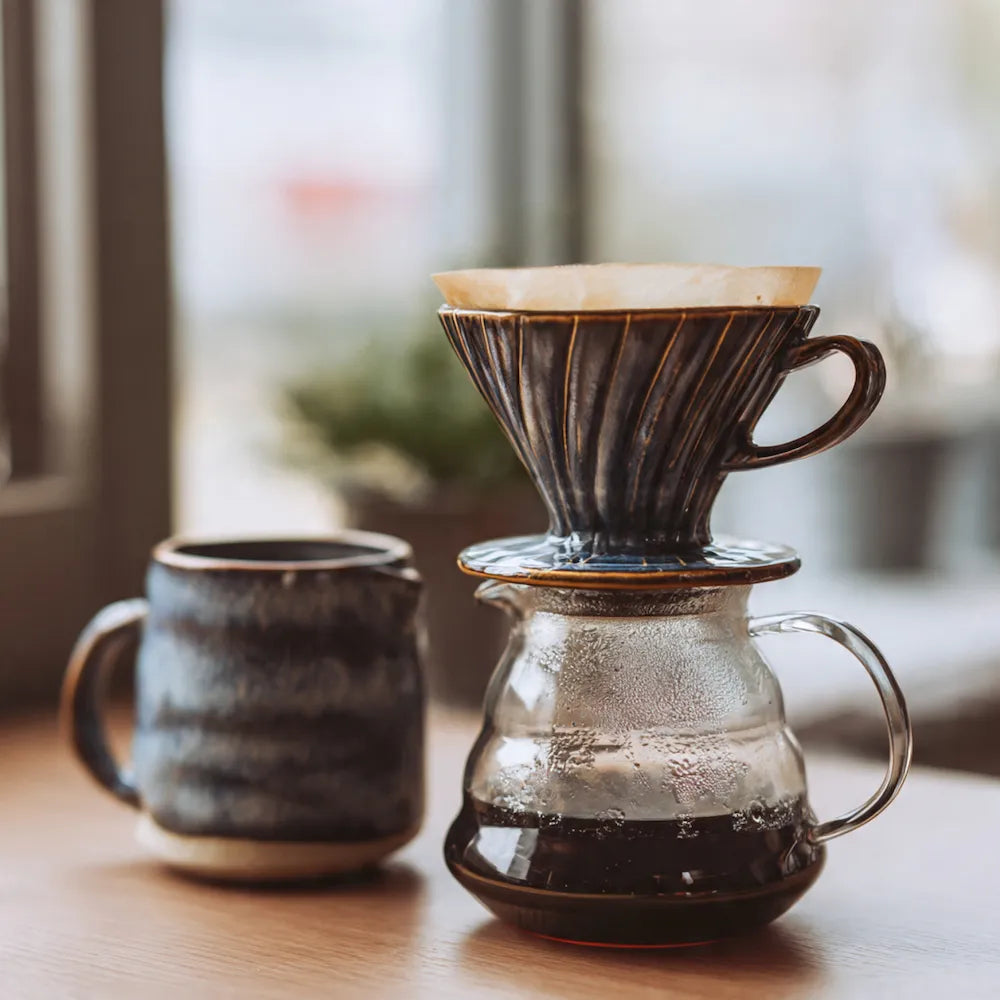 Coffee brewing setup with a glass carafe, coffee filter, and mug on a wooden surface.