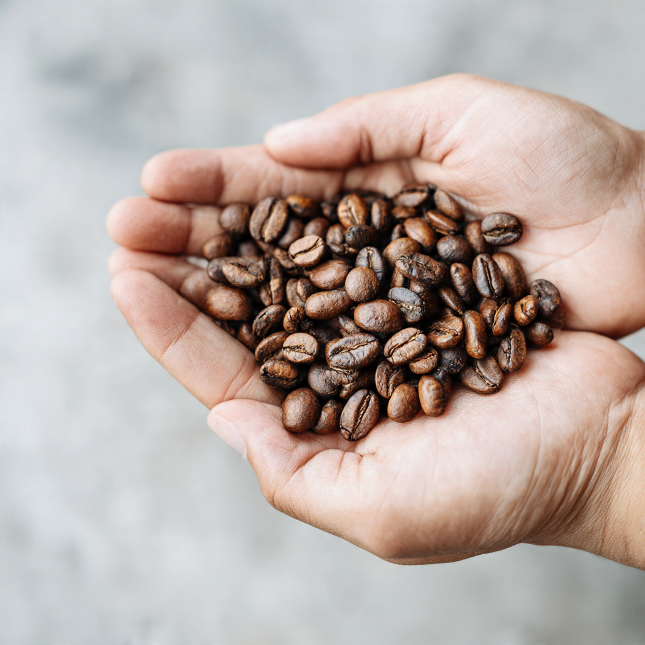 Hands holding a handful of dubai chocolate coffee beans against a neutral background