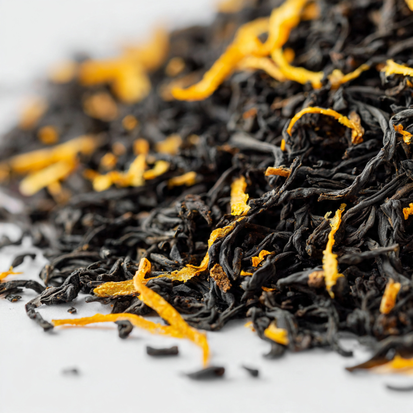 Close-up of black tea leaves with orange peel on a white background