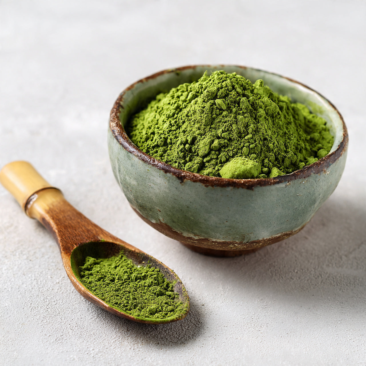 Matcha powder in ceramic bowl with bamboo scoop.