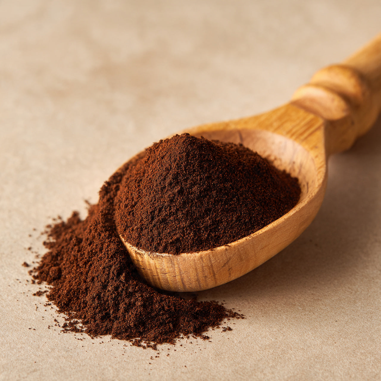 Wooden scoop filled with mocha coffee grounds on a beige background