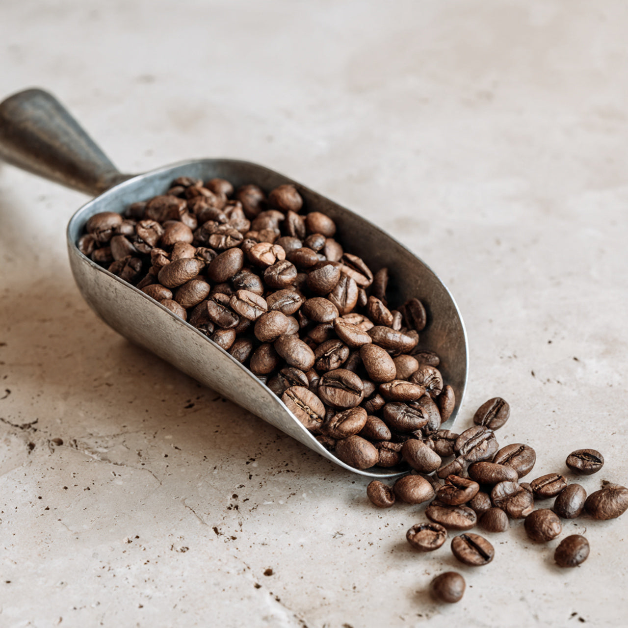 Metal scoop filled with hazelnut coffee beans on a light surface