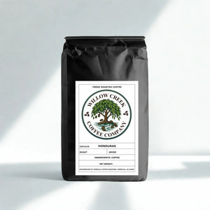 A black bag of Willow Creek Coffee Company fresh roasted coffee, Honduras, with a white label, standing on a light gray surface with soft diagonal shadows.