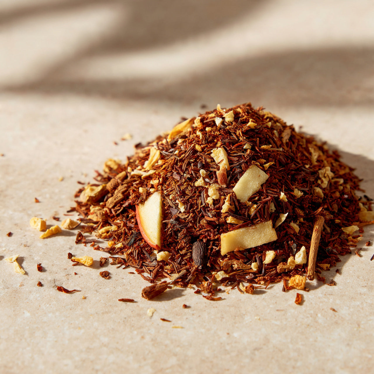 Heap of dried rooibos tea leaves with apple pieces on a beige surface
