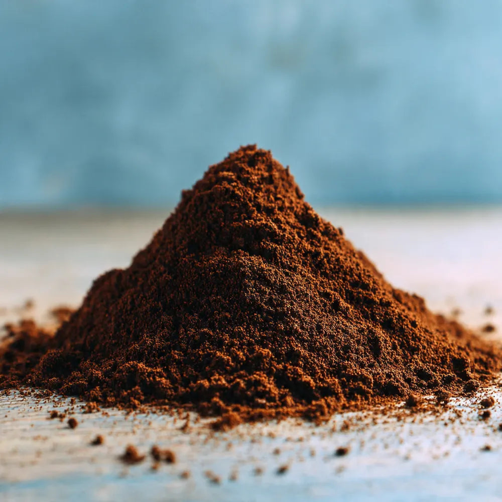 A small mound of sumatra ground coffee sits on a light surface with a soft blue-gray blurred background.